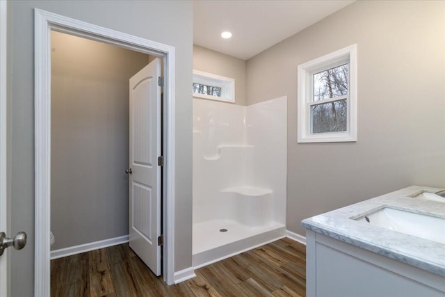 bathroom with wood finished floors, a walk in shower, baseboards, vanity, and toilet