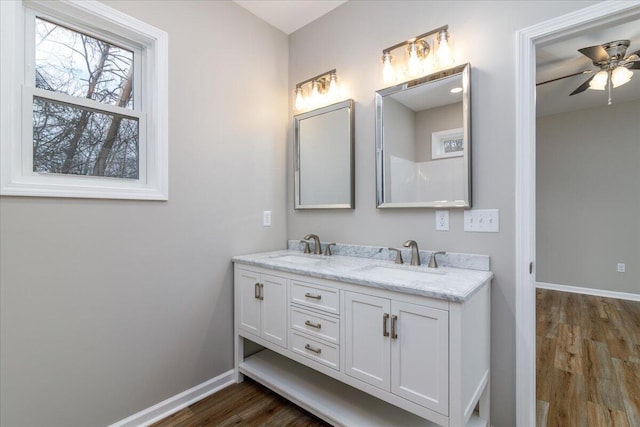 full bath featuring double vanity, a sink, baseboards, and wood finished floors