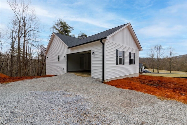view of side of property featuring driveway, a shingled roof, and a garage
