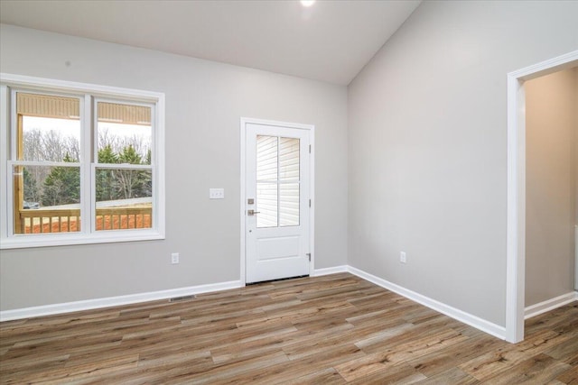 foyer entrance with baseboards, visible vents, wood finished floors, and lofted ceiling