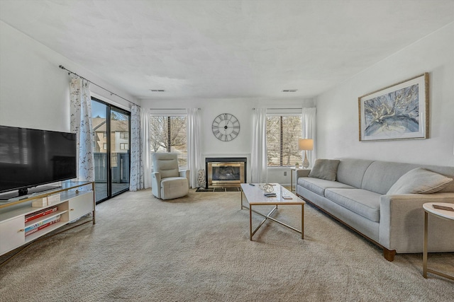 living area featuring a wealth of natural light, visible vents, a fireplace with flush hearth, and carpet flooring