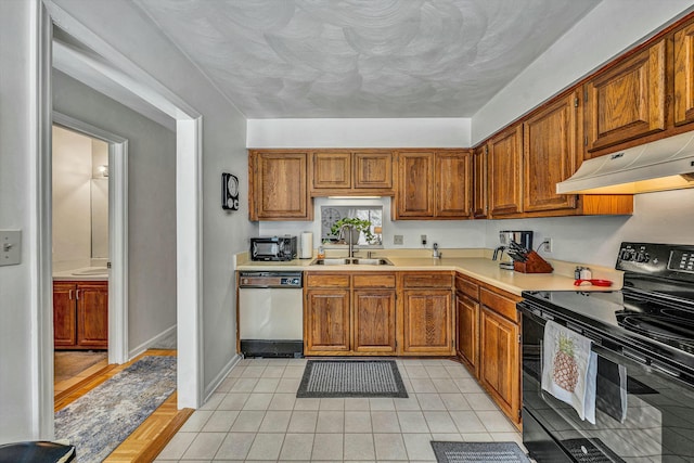 kitchen with brown cabinets, black appliances, under cabinet range hood, a sink, and light countertops