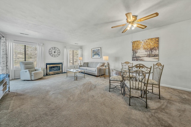 living room with visible vents, a fireplace with flush hearth, carpet, baseboards, and ceiling fan