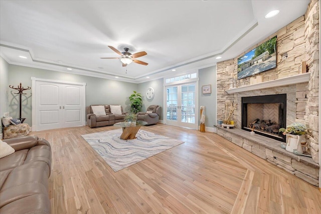 living area with baseboards, a raised ceiling, a stone fireplace, french doors, and light wood-type flooring