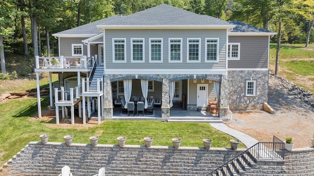 rear view of house featuring a patio, a shingled roof, stairs, a yard, and stone siding