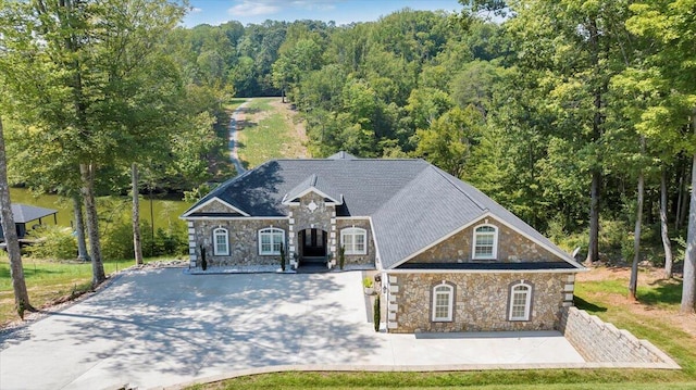 view of front of property with driveway, stone siding, and a forest view