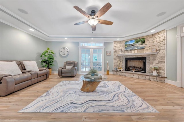 living room featuring recessed lighting, a fireplace, a tray ceiling, light wood finished floors, and crown molding