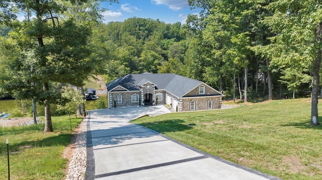 view of front facade with driveway, a garage, stone siding, a forest view, and a front lawn