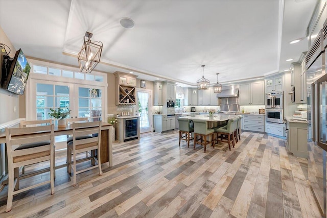 kitchen with beverage cooler, a breakfast bar, decorative light fixtures, an inviting chandelier, and wall chimney range hood