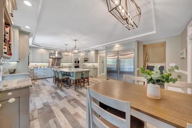 dining area featuring an inviting chandelier, a tray ceiling, crown molding, light wood-style floors, and recessed lighting