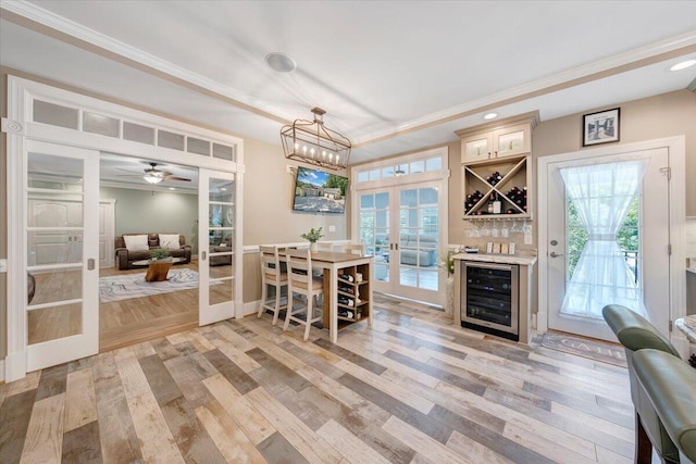 dining room with beverage cooler, light wood-style floors, french doors, ornamental molding, and a dry bar