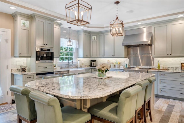 kitchen featuring hanging light fixtures, wall chimney range hood, a kitchen island, and glass insert cabinets