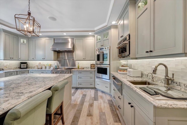 kitchen with wall chimney exhaust hood, appliances with stainless steel finishes, glass insert cabinets, and a warming drawer