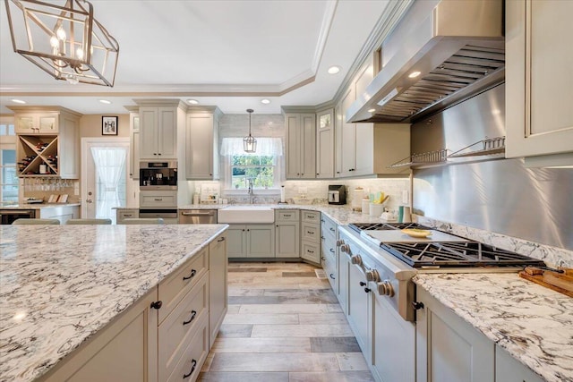 kitchen with a tray ceiling, wall chimney range hood, a sink, and pendant lighting