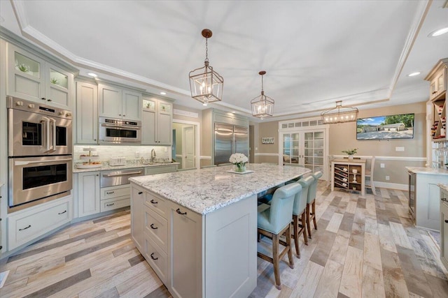 kitchen featuring decorative light fixtures, a kitchen island, appliances with stainless steel finishes, a warming drawer, and glass insert cabinets