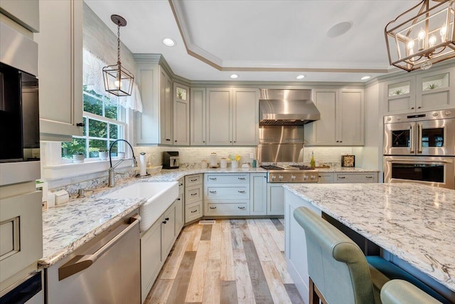 kitchen with wall chimney exhaust hood, a tray ceiling, glass insert cabinets, and pendant lighting