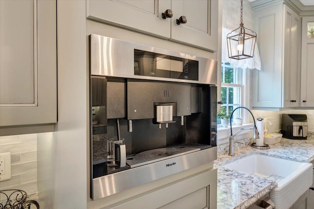 kitchen featuring light stone counters, pendant lighting, backsplash, white cabinets, and a sink