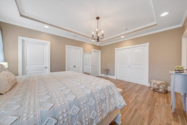 bedroom with light wood finished floors, a tray ceiling, two closets, and ornamental molding