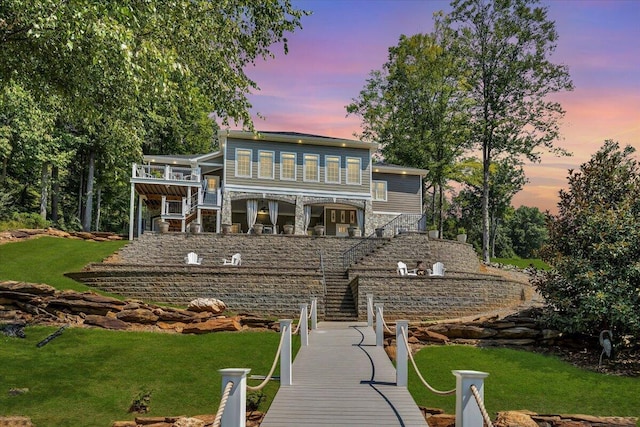 rear view of house featuring stone siding, stairway, and a lawn