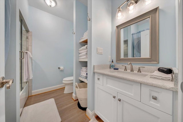 bathroom with toilet, bath / shower combo with glass door, wood finished floors, vanity, and baseboards