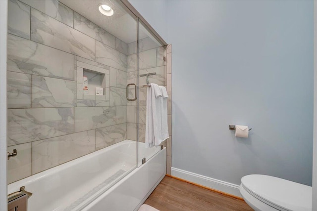 bathroom featuring bath / shower combo with glass door, wood finished floors, toilet, and baseboards