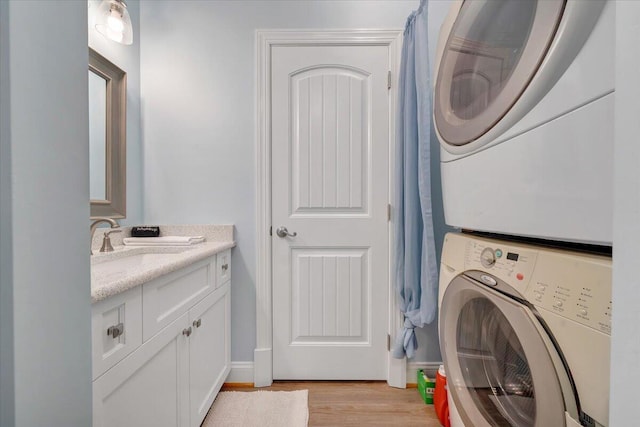 clothes washing area featuring light wood finished floors, cabinet space, baseboards, stacked washing maching and dryer, and a sink