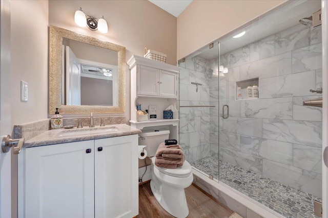 bathroom featuring wood finished floors, a shower stall, toilet, and vanity