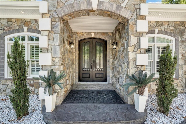 view of exterior entry featuring stone siding and french doors