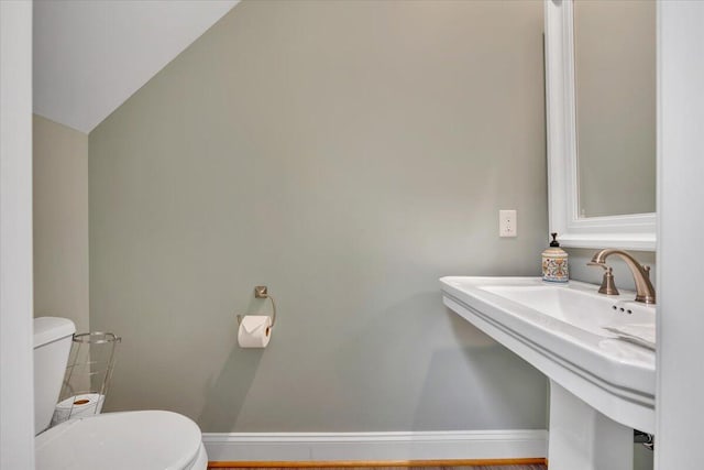 bathroom featuring toilet, baseboards, a sink, and lofted ceiling