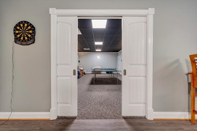 corridor featuring baseboards, a drop ceiling, and wood finished floors