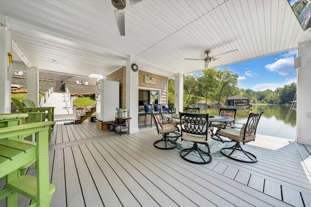 wooden terrace with a water view, outdoor dining area, and a ceiling fan