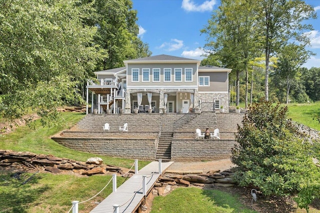 rear view of house with stone siding, stairway, and a lawn