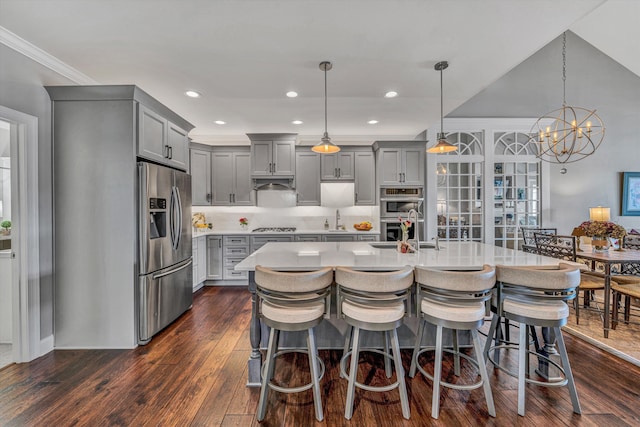 kitchen featuring dark wood finished floors, light countertops, appliances with stainless steel finishes, gray cabinets, and a kitchen bar