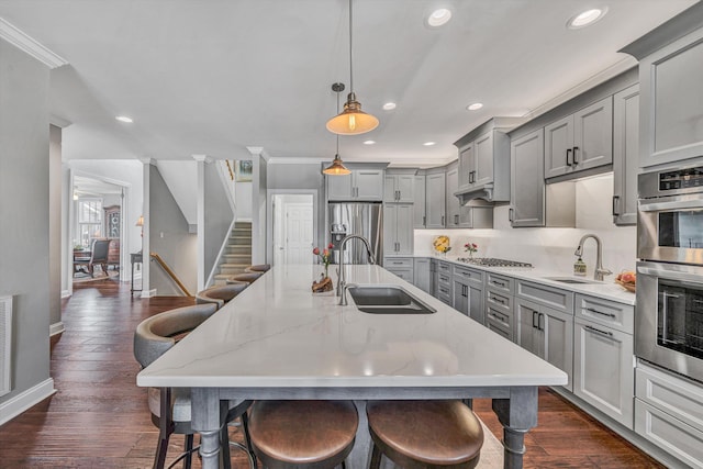 kitchen with a sink, appliances with stainless steel finishes, a kitchen bar, and gray cabinets