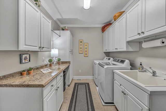 laundry area featuring cabinet space, baseboards, crown molding, washing machine and dryer, and a sink