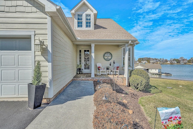 property entrance with a garage, covered porch, a shingled roof, a water view, and a yard