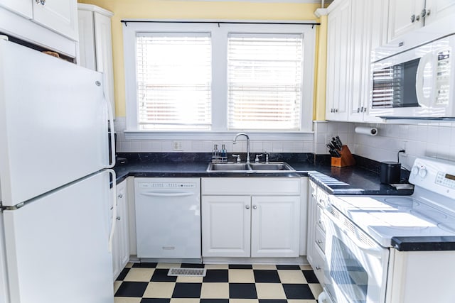 kitchen featuring dark countertops, white appliances, light floors, and a sink