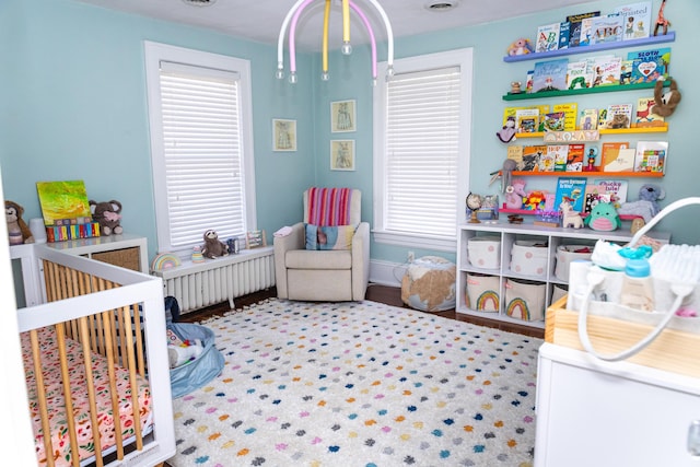 bedroom featuring a crib, radiator heating unit, and baseboards