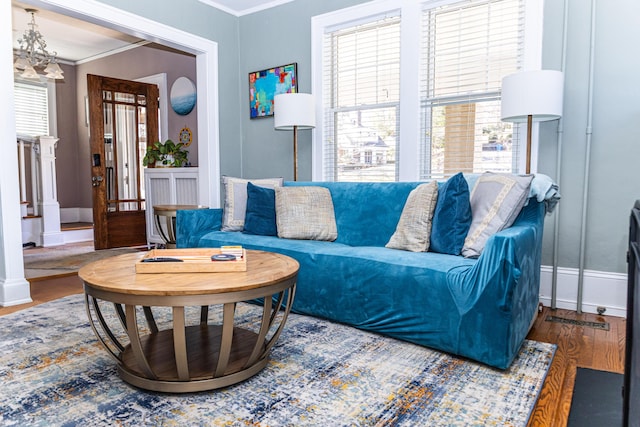 living area featuring ornamental molding, a notable chandelier, baseboards, and wood finished floors