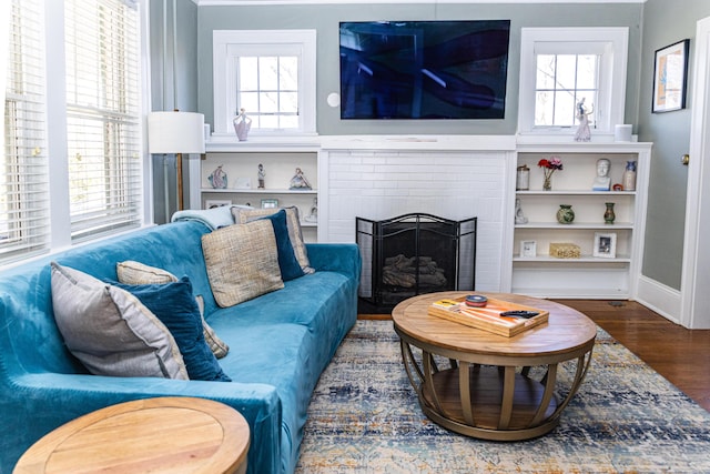 living area with a brick fireplace, baseboards, a wealth of natural light, and wood finished floors