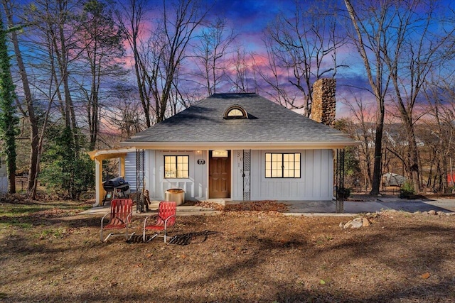 view of front of house with a shingled roof, a chimney, board and batten siding, and an outbuilding