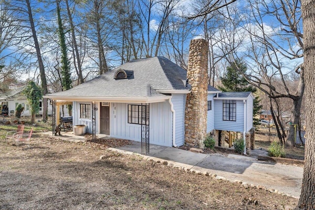 view of front of property with board and batten siding, a porch, a chimney, and a shingled roof