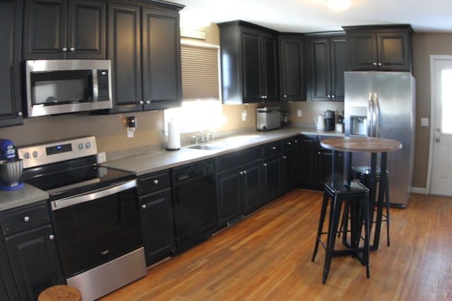 kitchen with light wood finished floors, dark cabinets, appliances with stainless steel finishes, and a sink