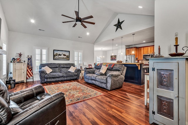 living area with dark wood-style floors, high vaulted ceiling, ceiling fan with notable chandelier, and visible vents