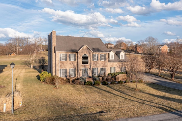 view of front facade featuring driveway, a chimney, and a front yard