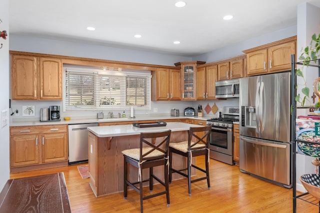 kitchen with light wood finished floors, stainless steel appliances, light countertops, a kitchen bar, and a sink