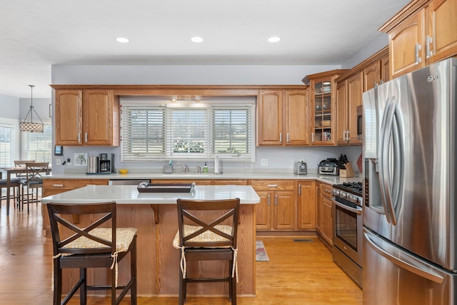 kitchen featuring stainless steel appliances, a breakfast bar, light wood-style floors, light countertops, and glass insert cabinets