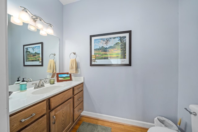 half bathroom with wood finished floors, vanity, toilet, and baseboards