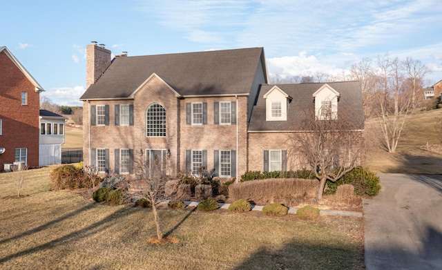 colonial-style house with brick siding, a front lawn, and a chimney