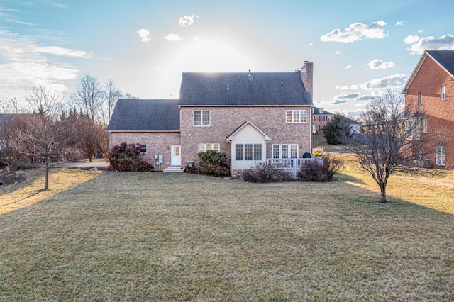 back of property with brick siding, a yard, a chimney, and roof with shingles